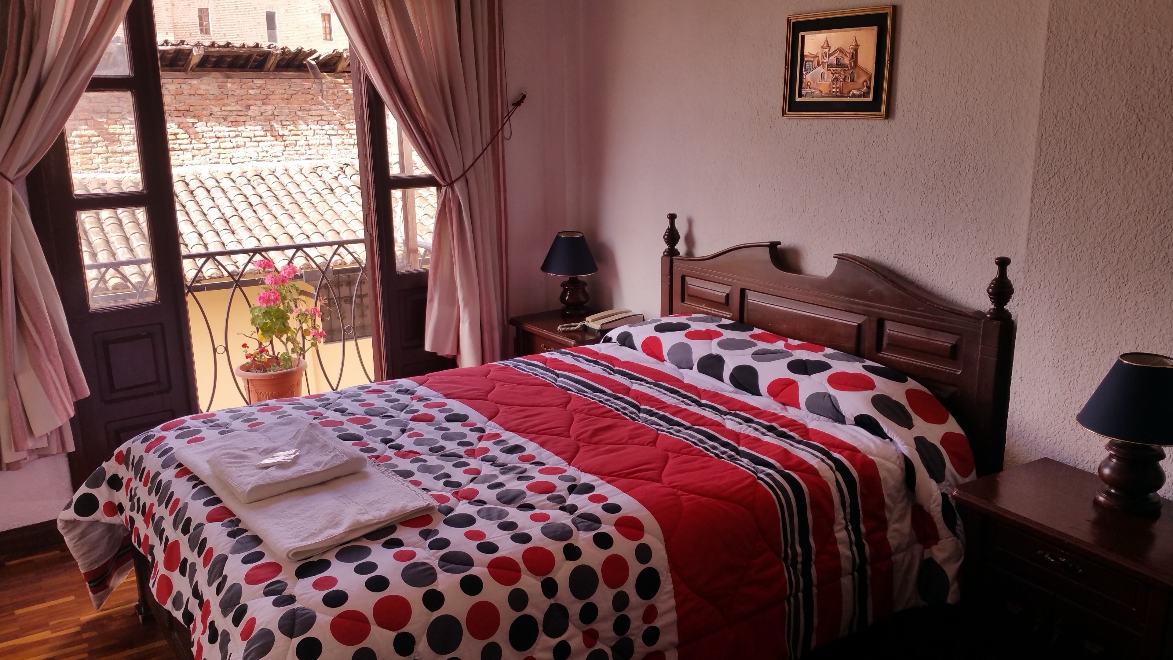 A hotel room with a bed, a nightstand, a lamp, a potted plant, and a window with curtains.