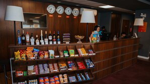 Mostrador de recepción de hotel con relojes, televisor y diversos aperitivos y bebidas.