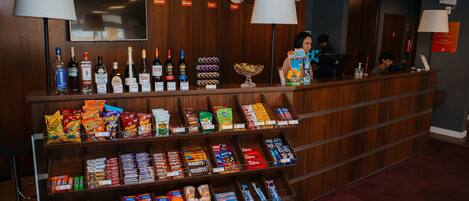 A hotel reception desk with clocks, a TV, and various snacks and beverages.