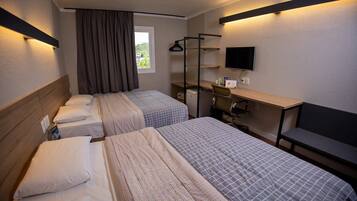A hotel room with two beds, a desk with a chair, a TV, and a window with curtains.