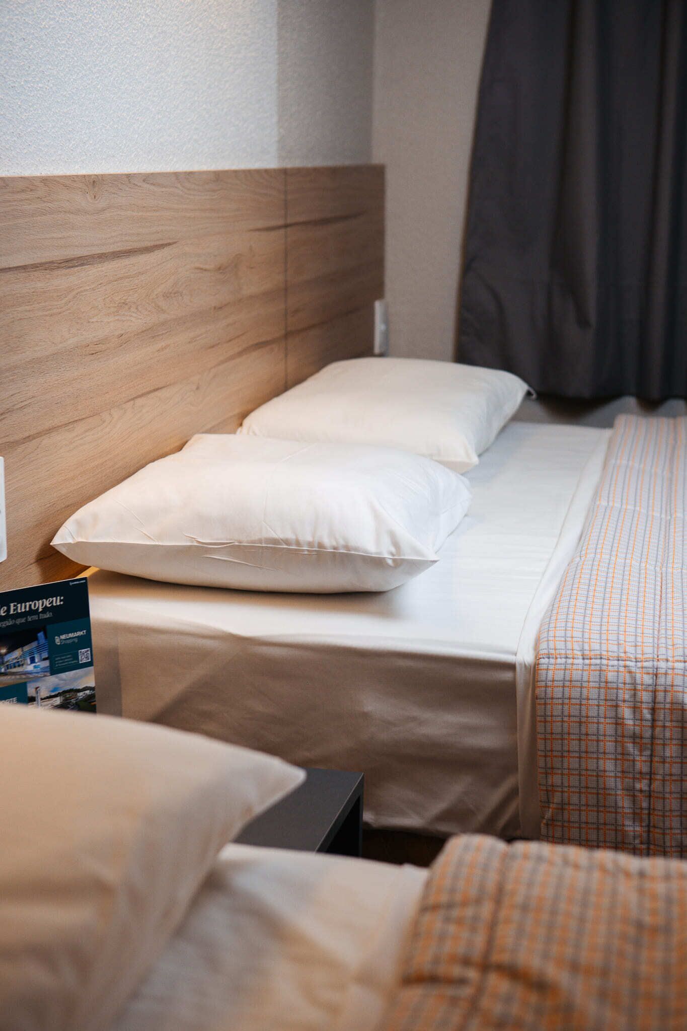 Una habitación de hotel con cabecera de madera, cama con ropa blanca y manta a cuadros.