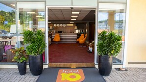 Entrada de un hotel con mostrador de recepción, dos sillones naranja y plantas en macetas.