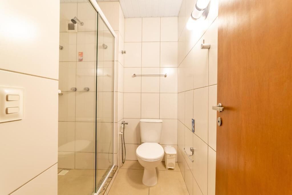 A bathroom with a glass shower enclosure, a toilet, and a wooden door.