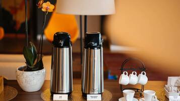 A table with two stainless steel thermos bottles, a small potted orchid, a tea set, and a sugar packet box.