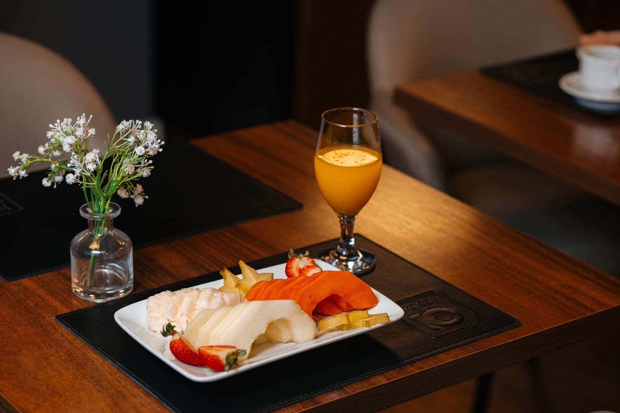 A dining table with a plate of food, a glass of orange juice, and a small vase with flowers.