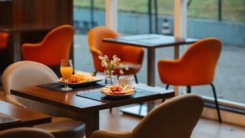 Un comedor con una mesa dispuesta para el desayuno, que incluye un plato de comida, un vaso de jugo de naranja y una taza de café.