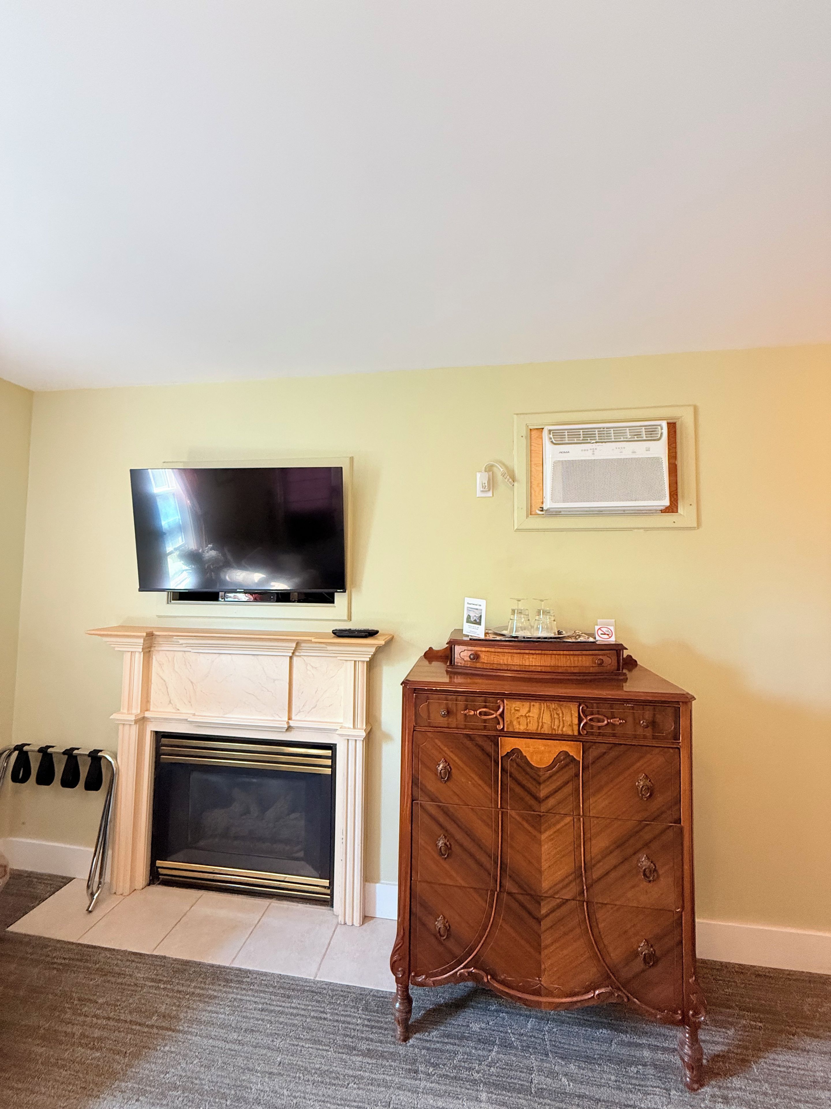 Una sala de estar con un televisor de pantalla plana sobre una chimenea, un mueble de madera y un aire acondicionado instalado en la pared.