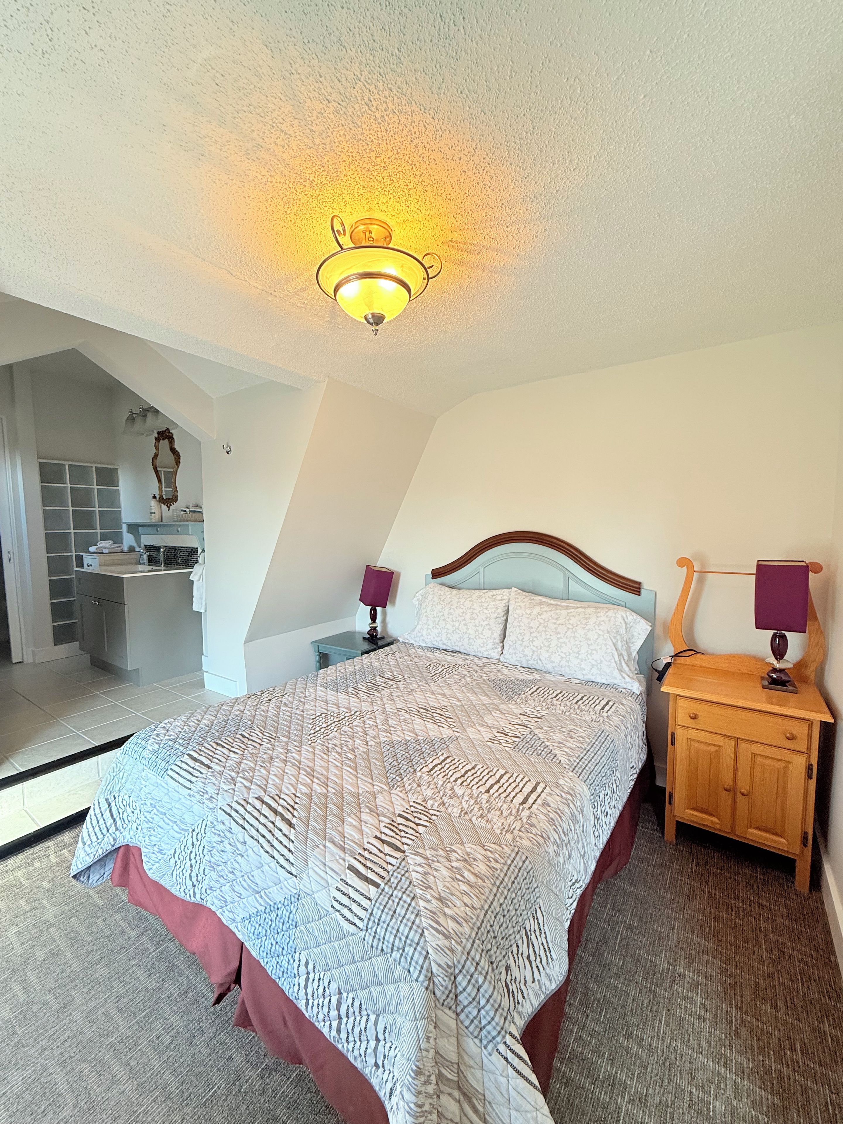 A bedroom with a large bed, a wooden nightstand, a bedside lamp, and a ceiling light fixture.