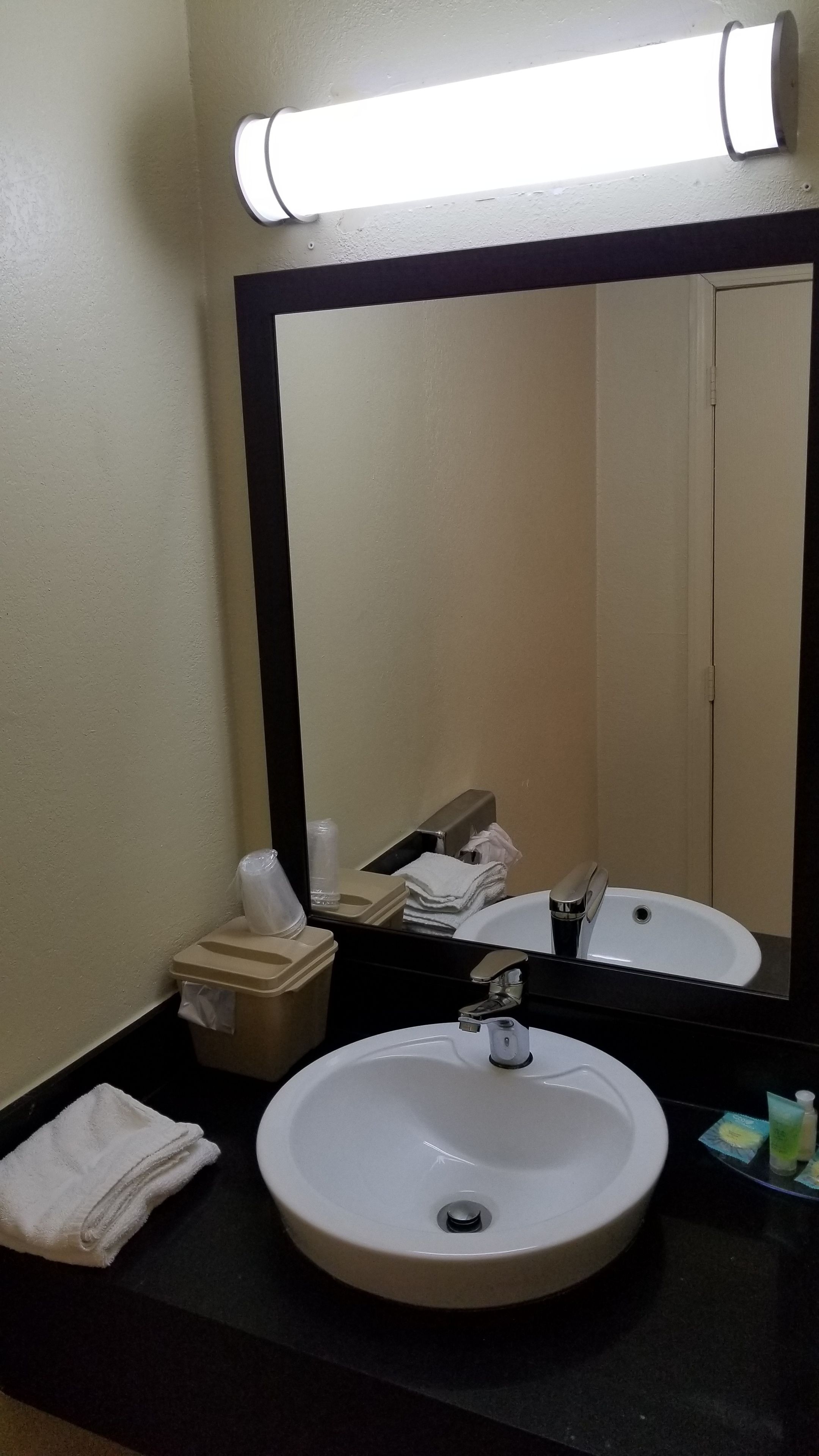 A bathroom with a round sink, a mirror, and a towel dispenser.