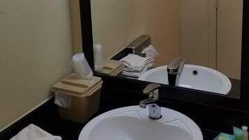A bathroom with a round sink, a mirror, and a towel dispenser.