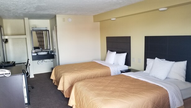 Ein Hotelzimmer mit zwei Betten, einem Schreibtisch, einem Spiegel und einem Waschbecken.