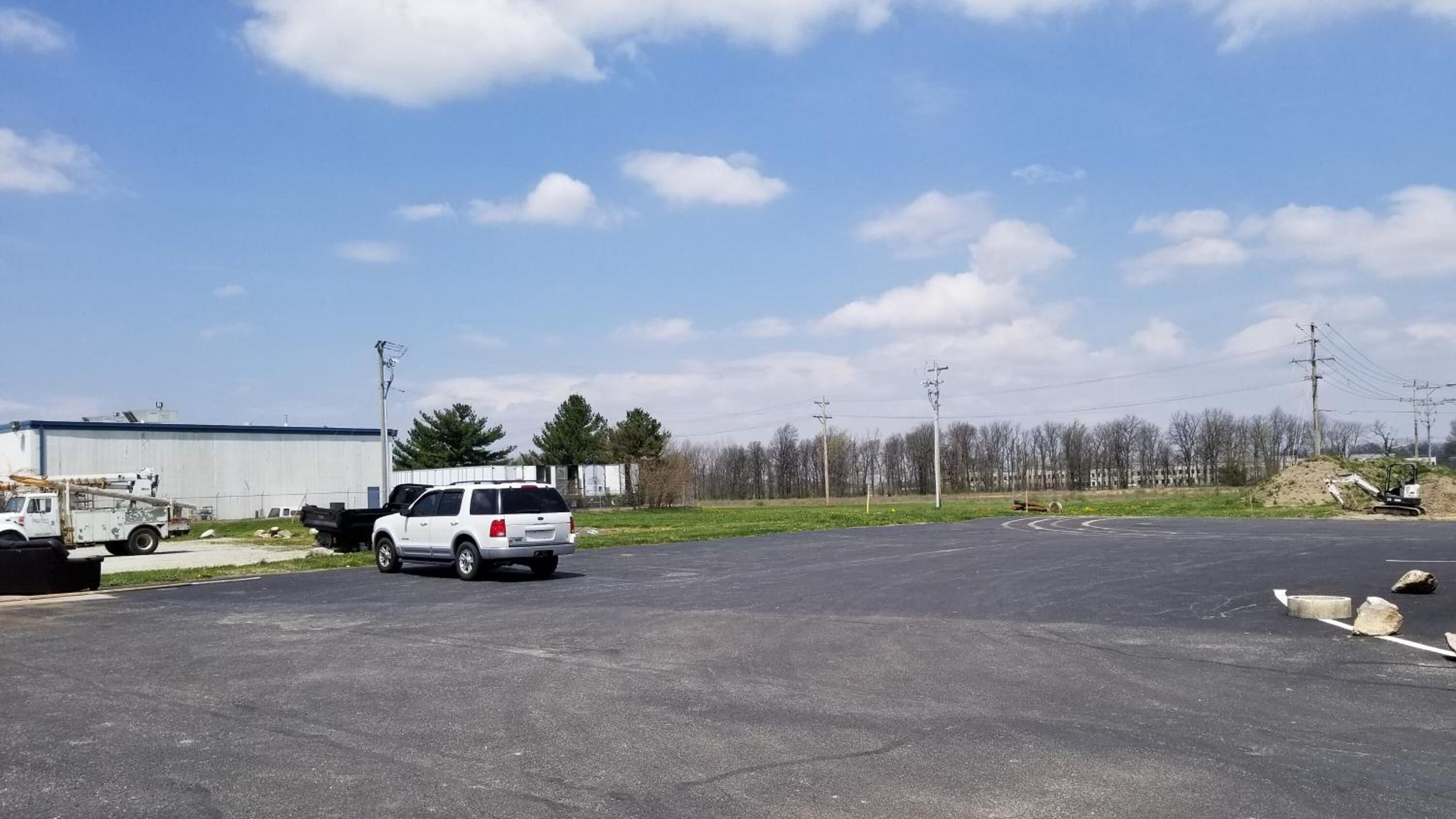 A parking lot with a white SUV, a utility truck, and construction equipment.