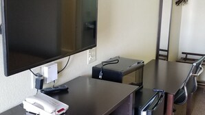 Ein Hotelzimmer mit Flachbildfernseher an der Wand, einem Schreibtisch mit Telefon, einem Spiegel und einem Sessel.