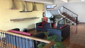 Un vestíbulo amplio con una escalera, sofás de cuero, una planta en maceta y jarrones decorativos en estanterías.