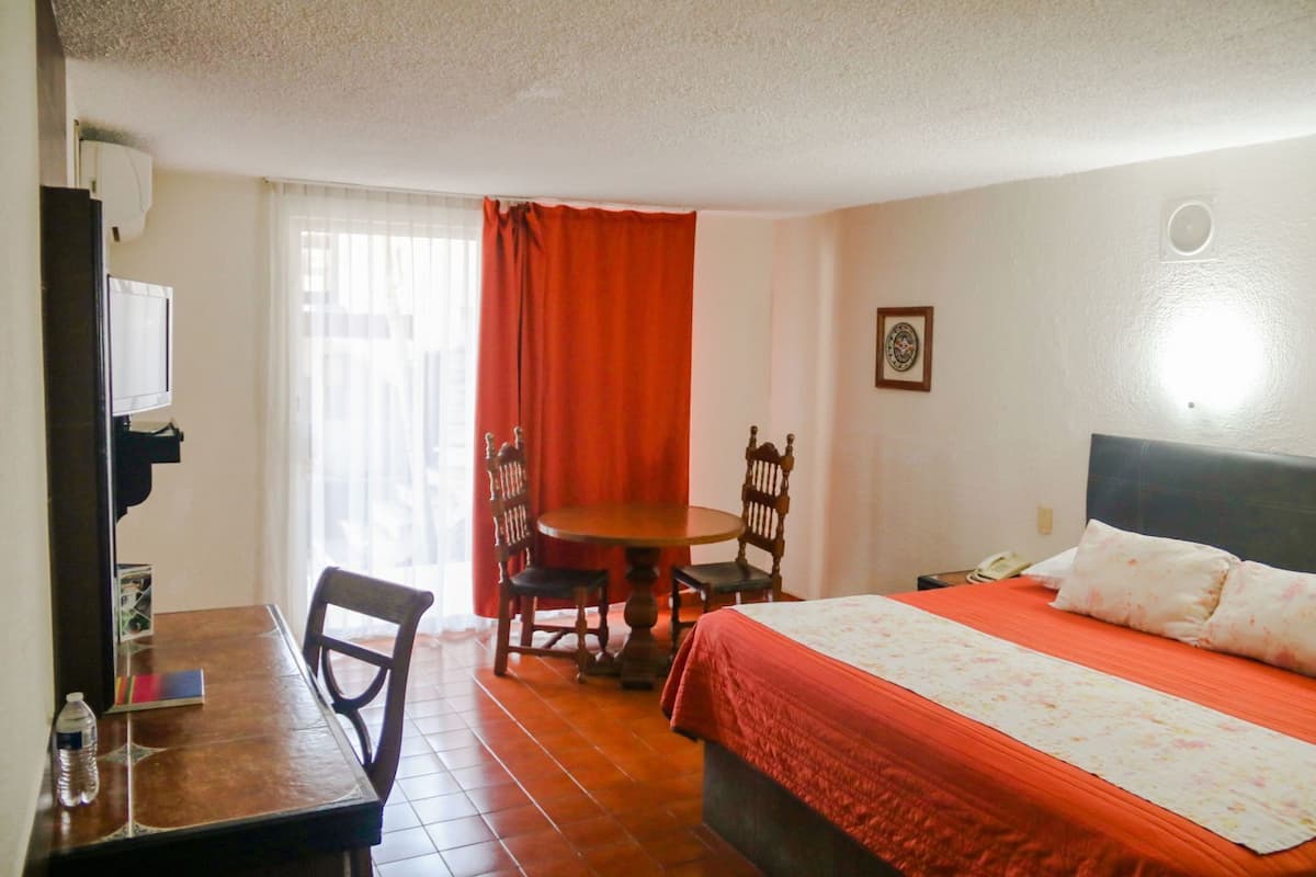 Habitación de hotel con cama, escritorio con sillas, televisor y ventana con cortinas.