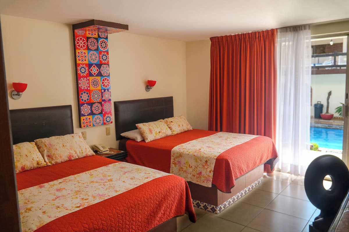 Habitación de hotel con dos camas, una cortina roja, un papel tapiz decorado y vistas a una piscina.