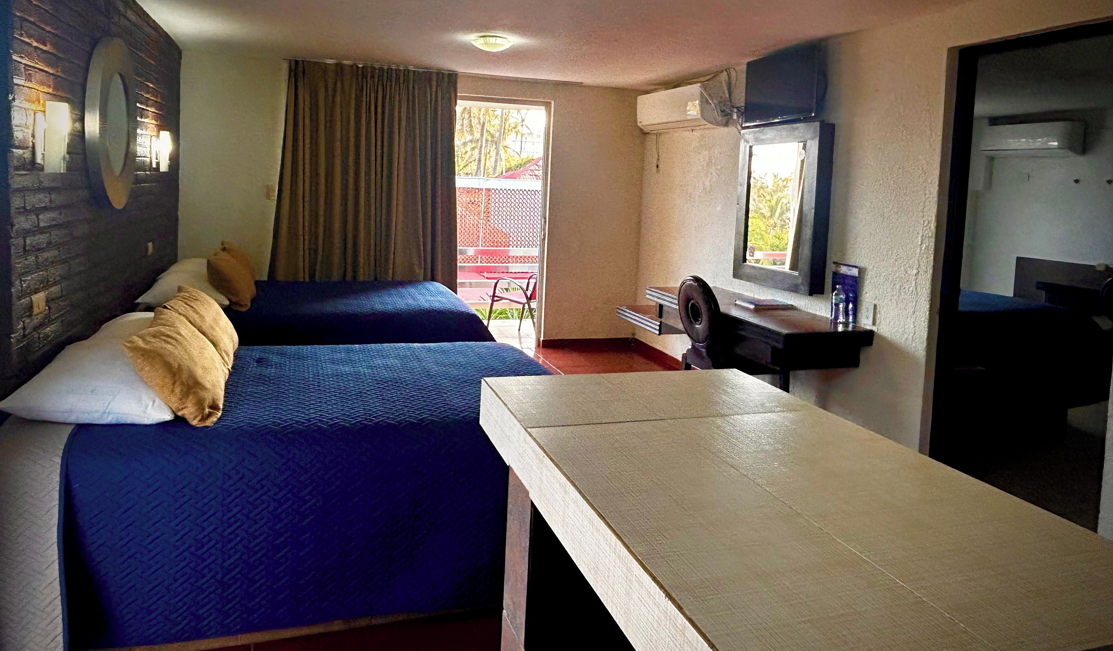 Una habitación con dos camas, un escritorio, una silla, un ventanal y una puerta.