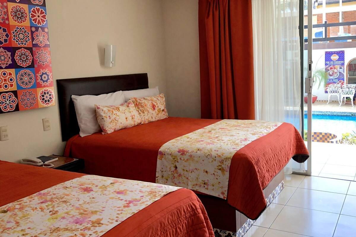 Habitación de hotel con dos camas, vista a una piscina y balcón con mobiliario exterior.