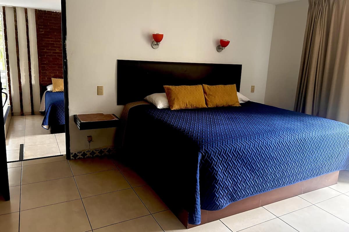 Habitación de hotel con una cama grande, una mesita de noche, un espejo y una lámpara de pared roja.