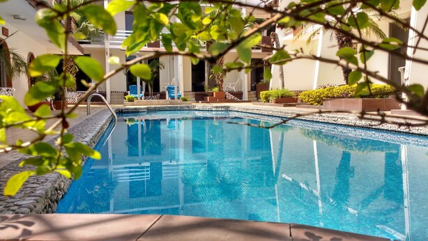 Una piscina con agua azul cristalina, rodeada de baldosas de piedra y plantas en macetas.