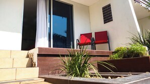 Un edificio moderno con un amplio escaparate de vidrio, una silla roja y un pequeño jardín con plantas.