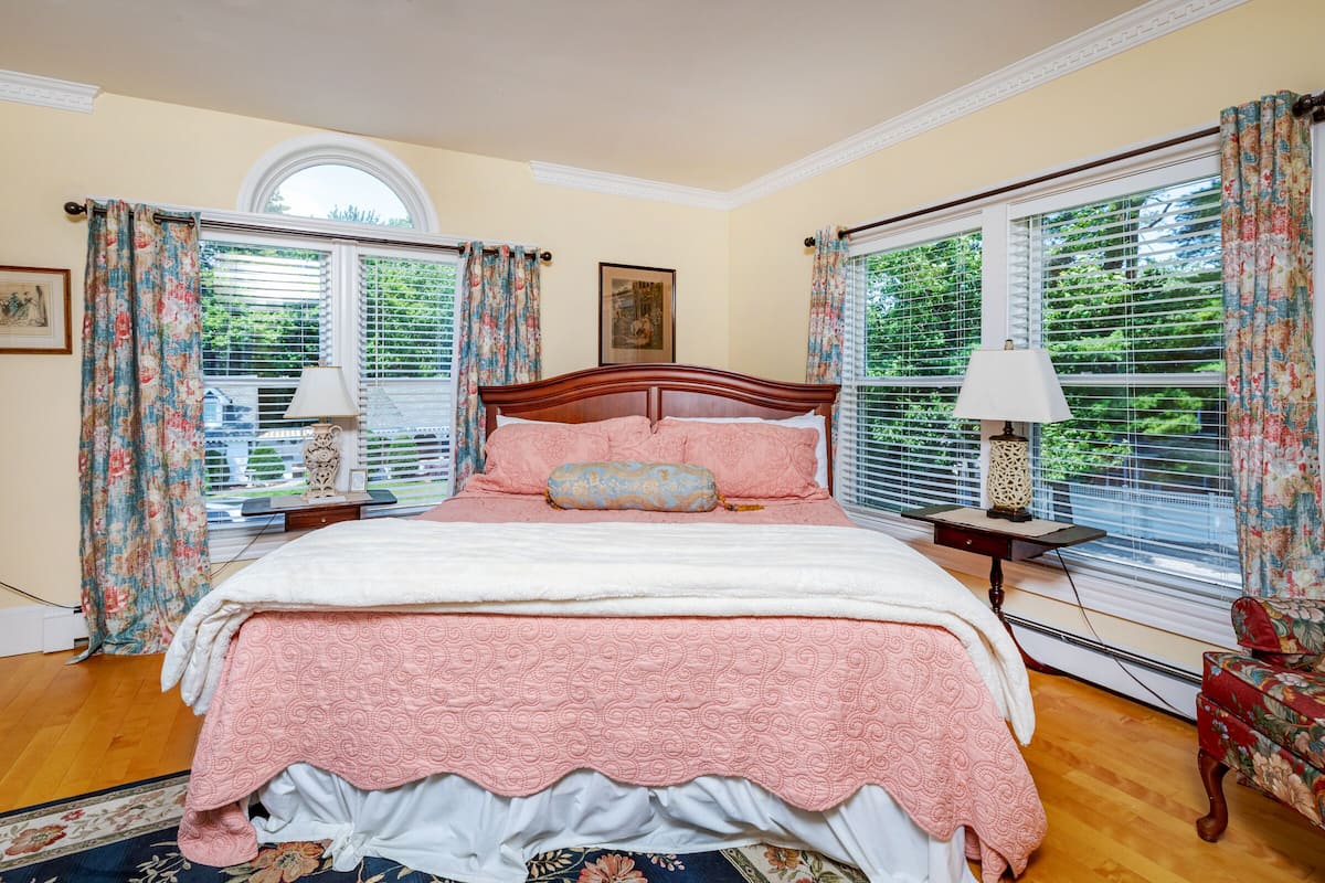 A bedroom with a large bed, floral curtains, and a view of greenery outside.