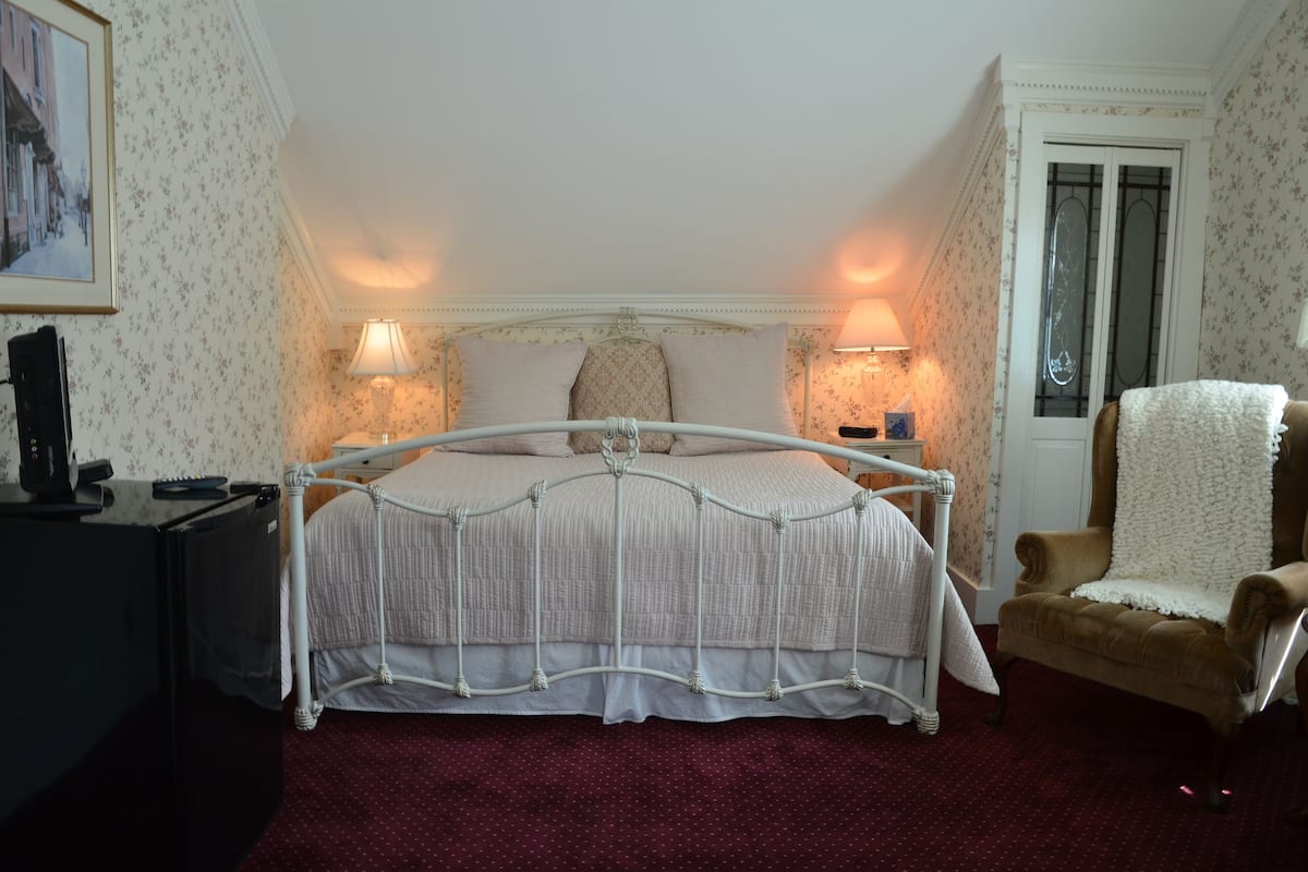 A bedroom with a bed, bedside lamps, a chair, a desk, and a door.