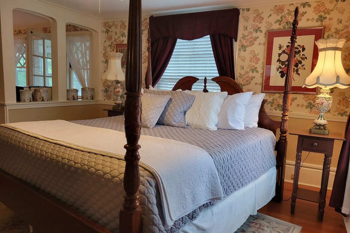 A four-poster bed with a quilted bedspread, a wooden headboard, and a nightstand with a lamp.