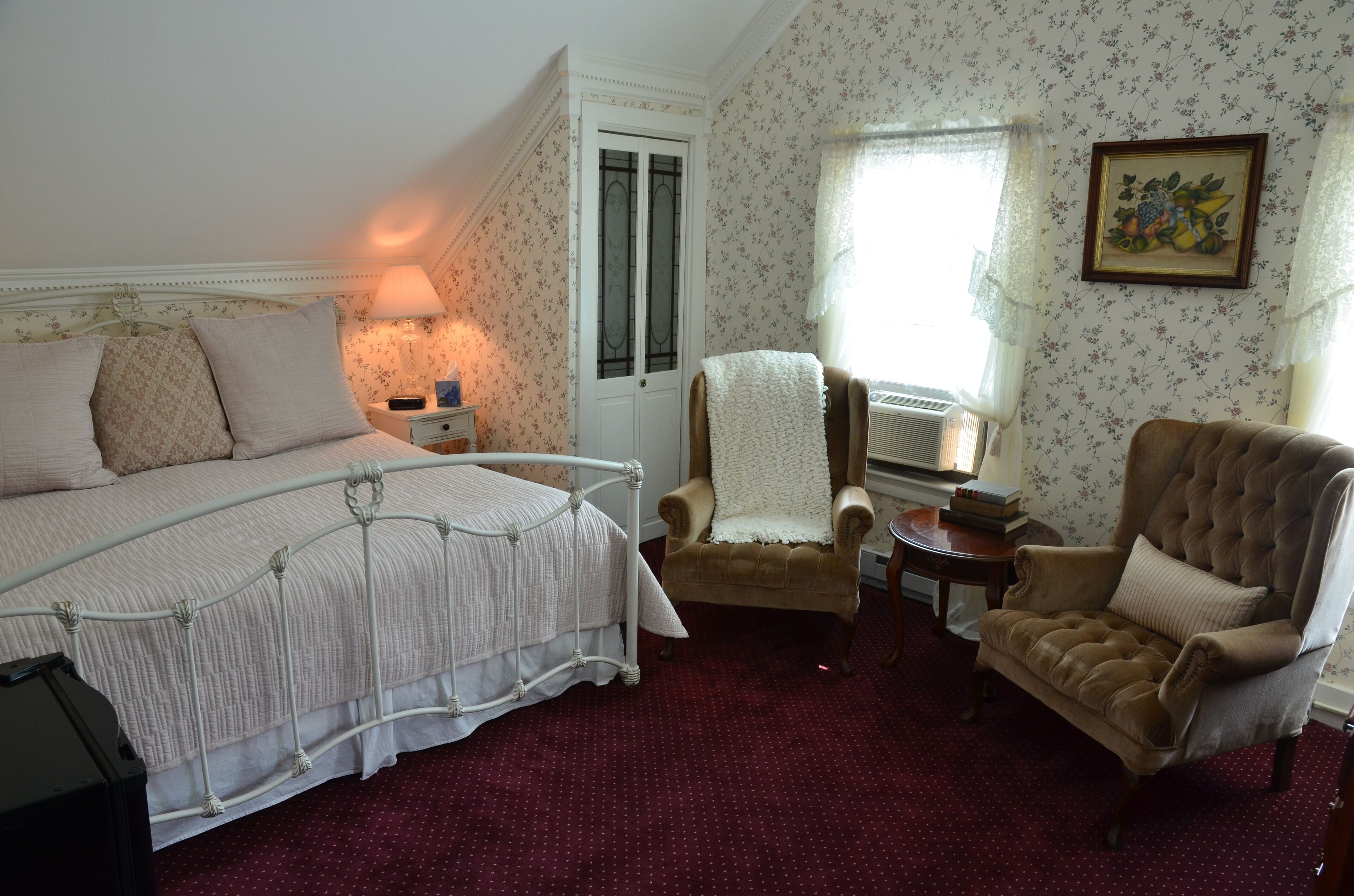 A bedroom with a bed, a chair, a nightstand, a lamp, and a door.