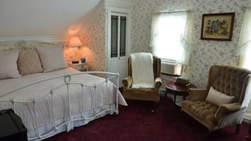 A bedroom with a bed, a chair, a nightstand, a lamp, and a door.
