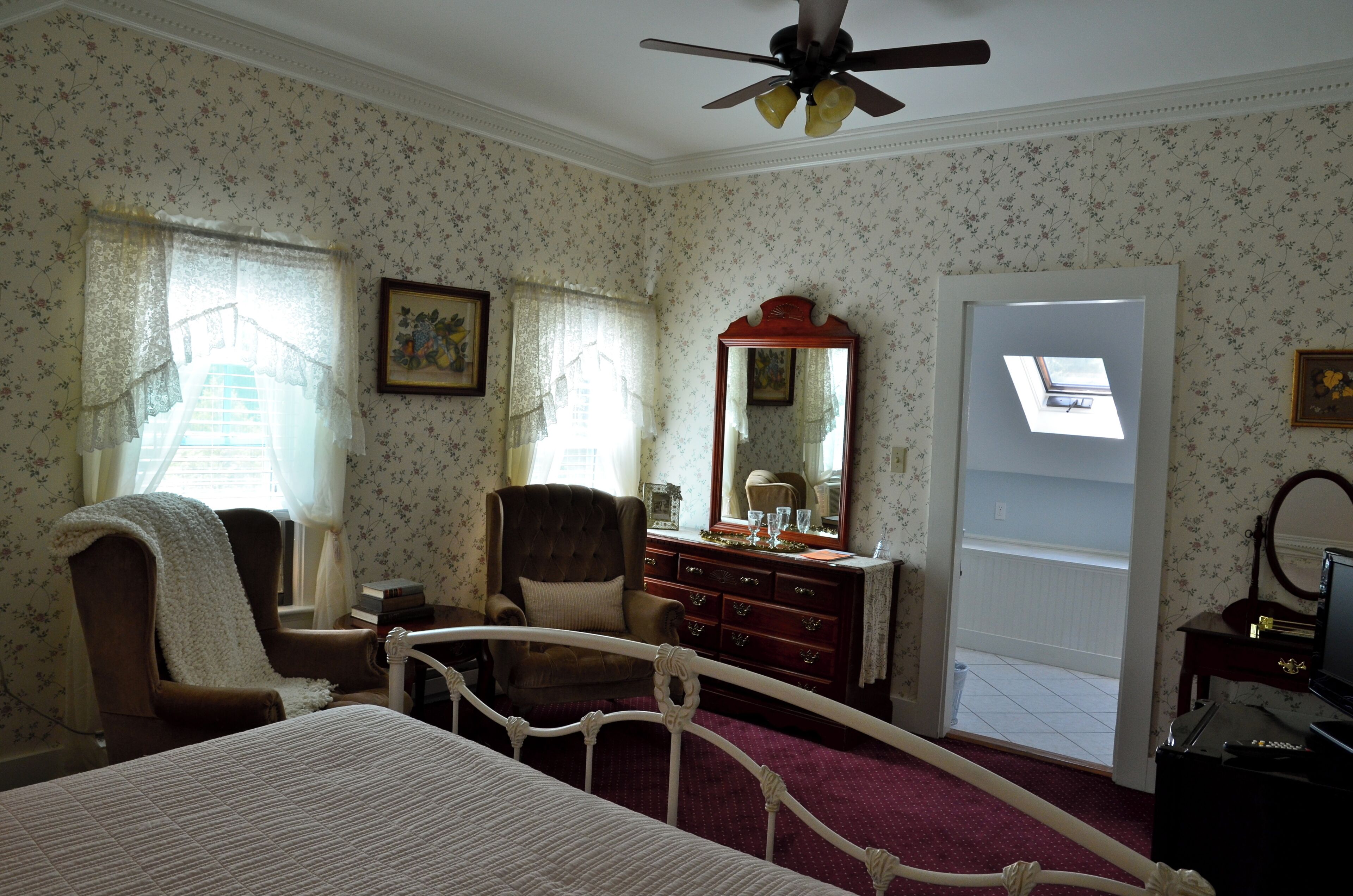 A bedroom with a bed, a chair, a dresser, a mirror, and a ceiling fan.