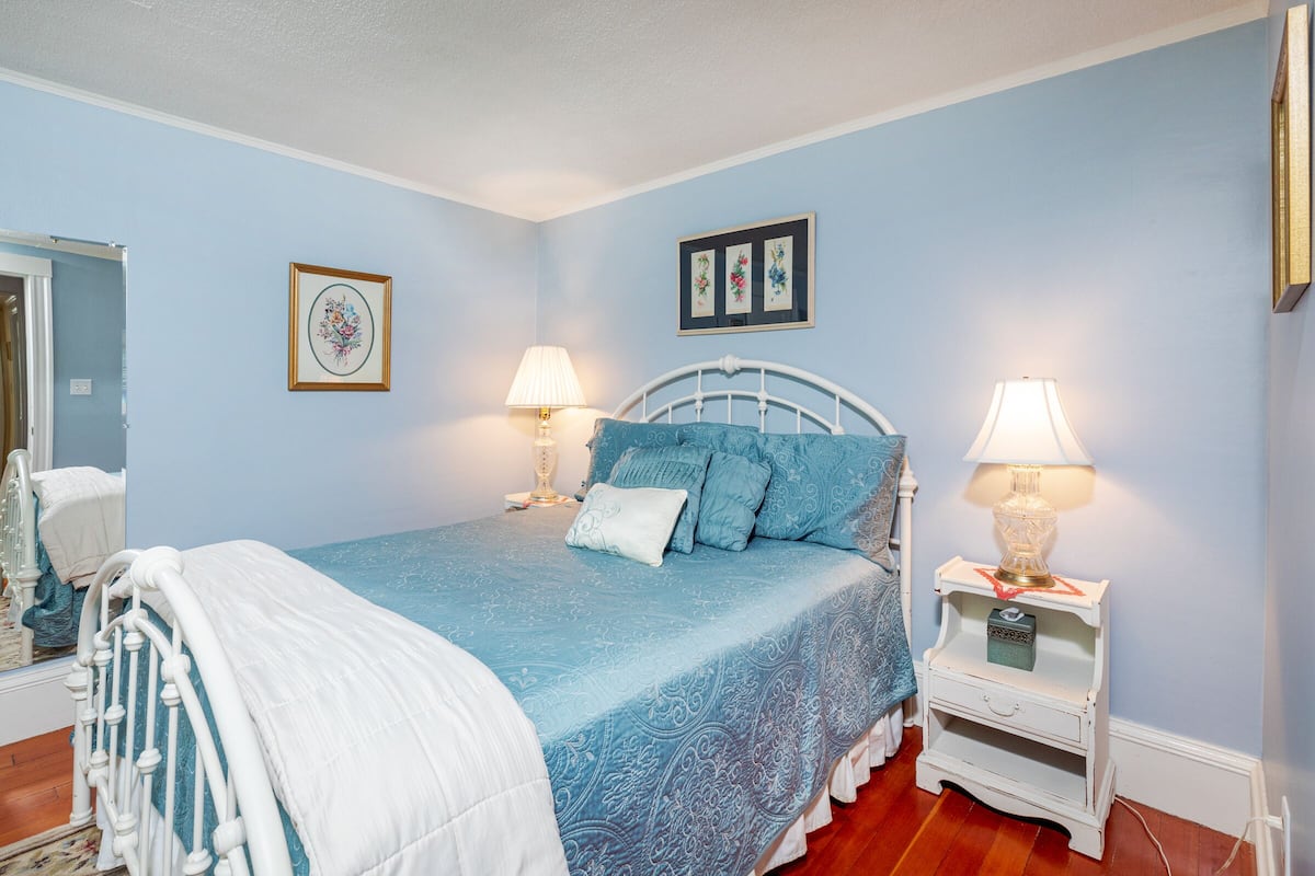 A bedroom with a bed, two bedside tables with lamps, a mirror, and framed artwork on the wall.