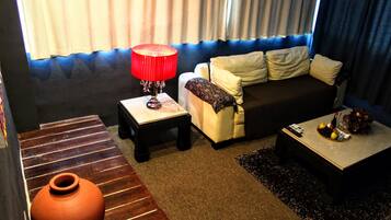 Uma sala de estar com sofá, mesa de centro, luminária vermelha, vaso e tapete estampado.