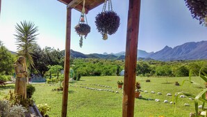 A garden with a wooden pergola, hanging flower baskets, a statue, and a view of mountains in the background. - Nativa Posada & Spa (Montemorelos)