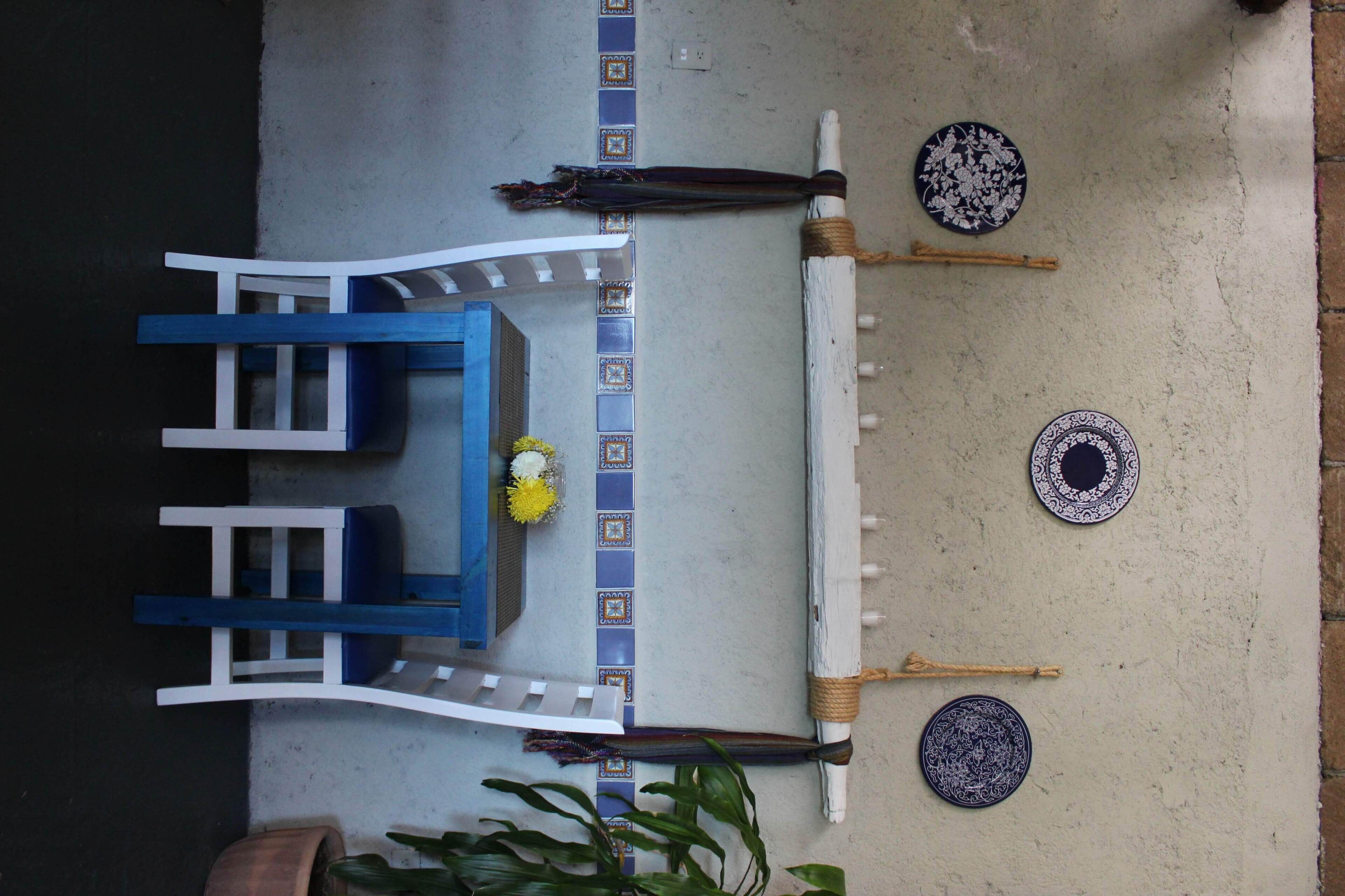 Un comedor con una mesa azul y sillas blancas, un pequeño arreglo floral y platos decorativos en la pared.