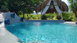A clear blue pool with a fish-shaped water feature, surrounded by lush greenery and a thatched-roof structure. - Nativa Posada & Spa (Montemorelos)