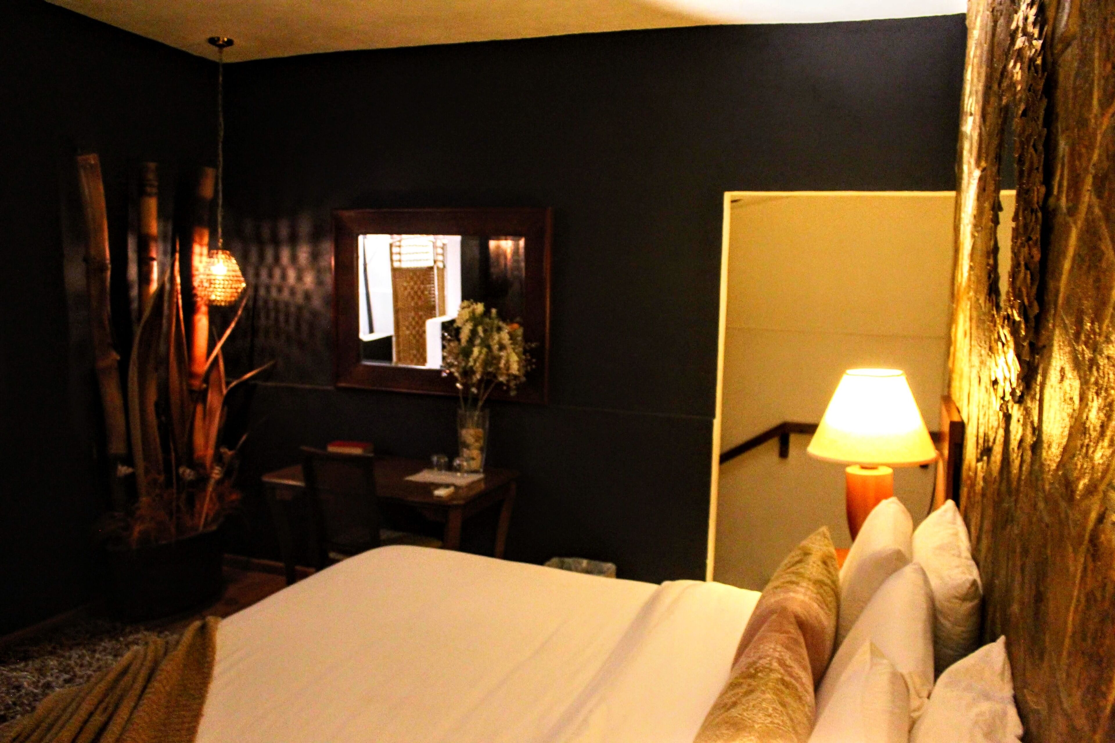 Une chambre d’hôtel avec un lit, un bureau, une chaise, une lampe et un miroir.