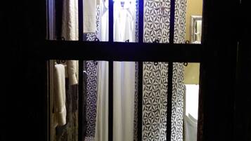 Vista a través de una ventana con barrotes que da a un baño con cortinas estampadas, un perchero y un espejo.