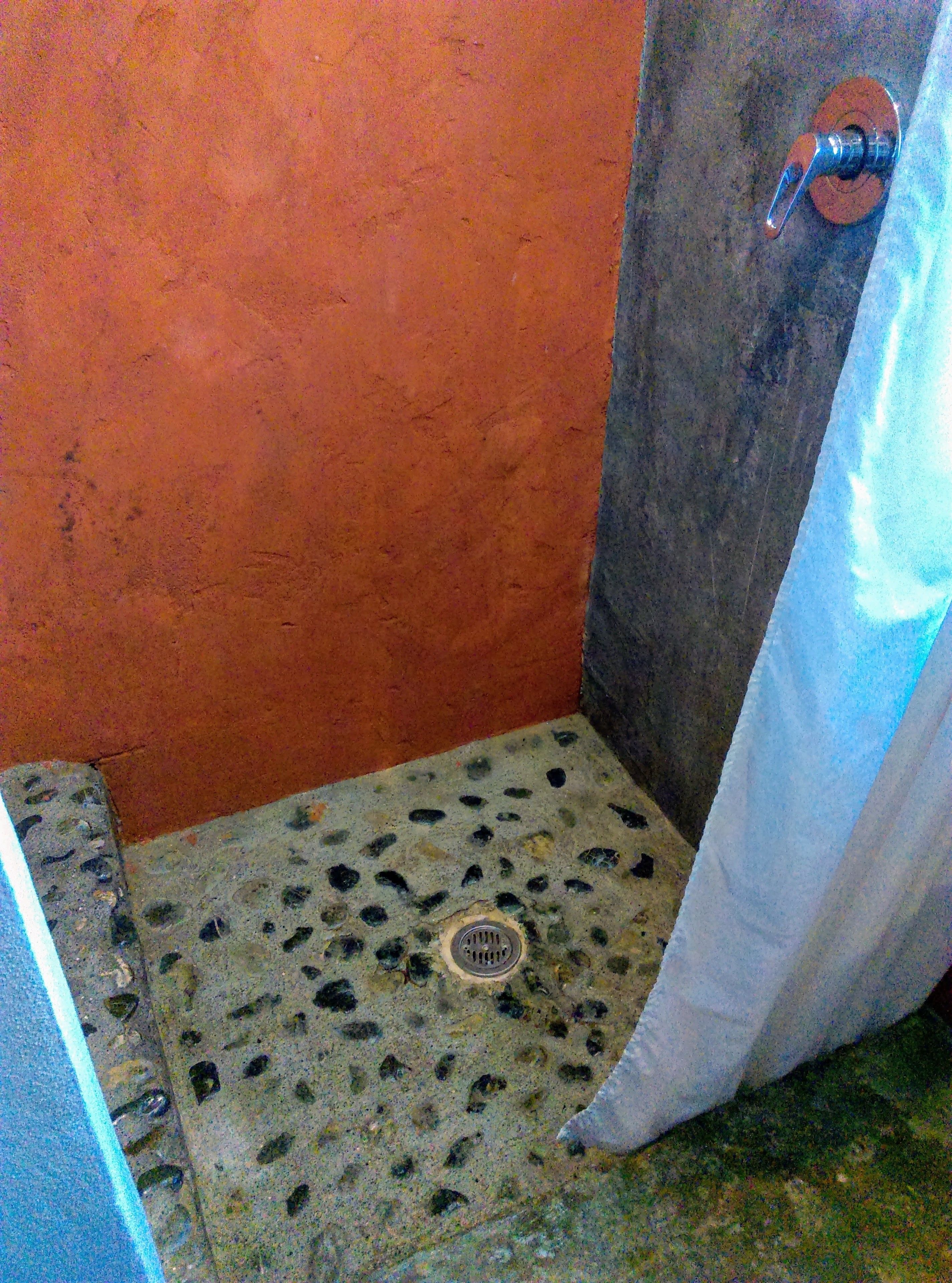 A small, tiled shower area with a drain, a metal faucet, and a curtain.