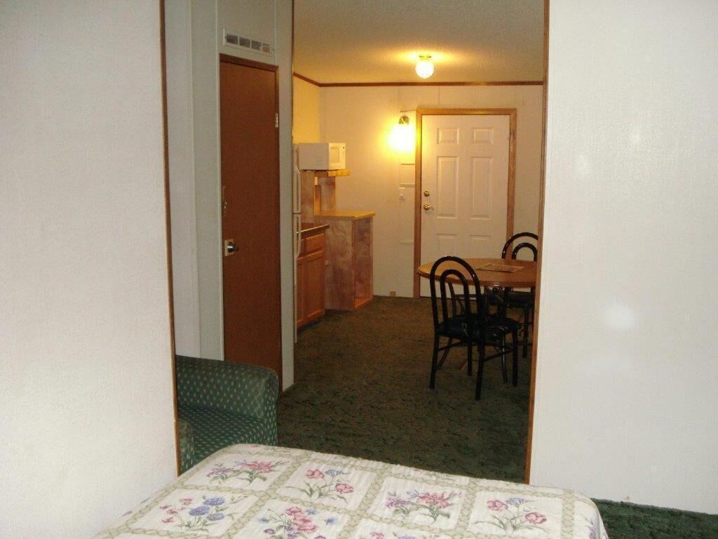 Una habitación con una cama, un escritorio pequeño, una silla y una puerta que da a otra habitación.