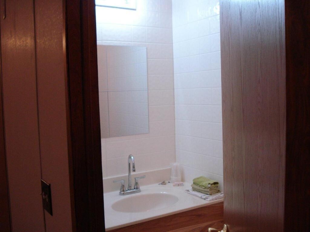 Un baño con lavamanos blanco, un espejo y una puerta de madera.
