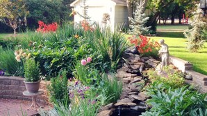 A garden with a small pond, various plants, and a statue. - McDougall Lane Bed & Breakfast (Drumheller)