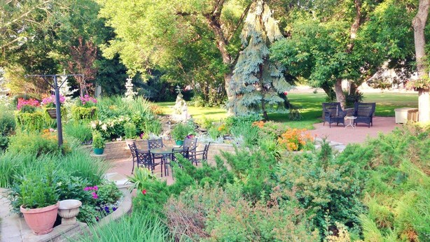 A garden patio with outdoor furniture, surrounded by lush greenery and flowering plants. - McDougall Lane Bed & Breakfast (Drumheller)