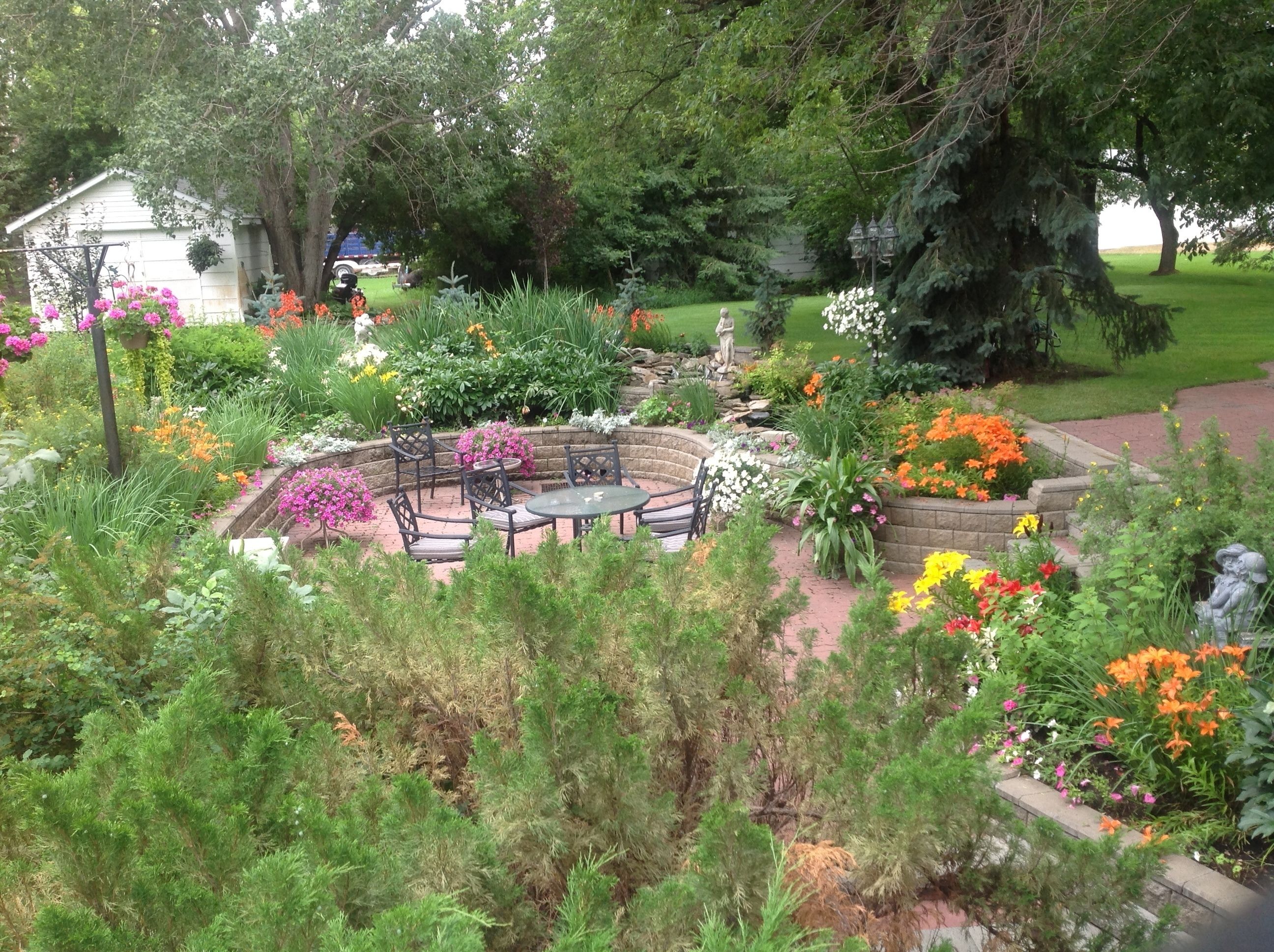 A garden with a circular seating area, surrounded by various plants and flowers.