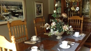 A dining table set with white cups and saucers, a vase with flowers, and a wooden chair with a woven seat. - McDougall Lane Bed & Breakfast (Drumheller)
