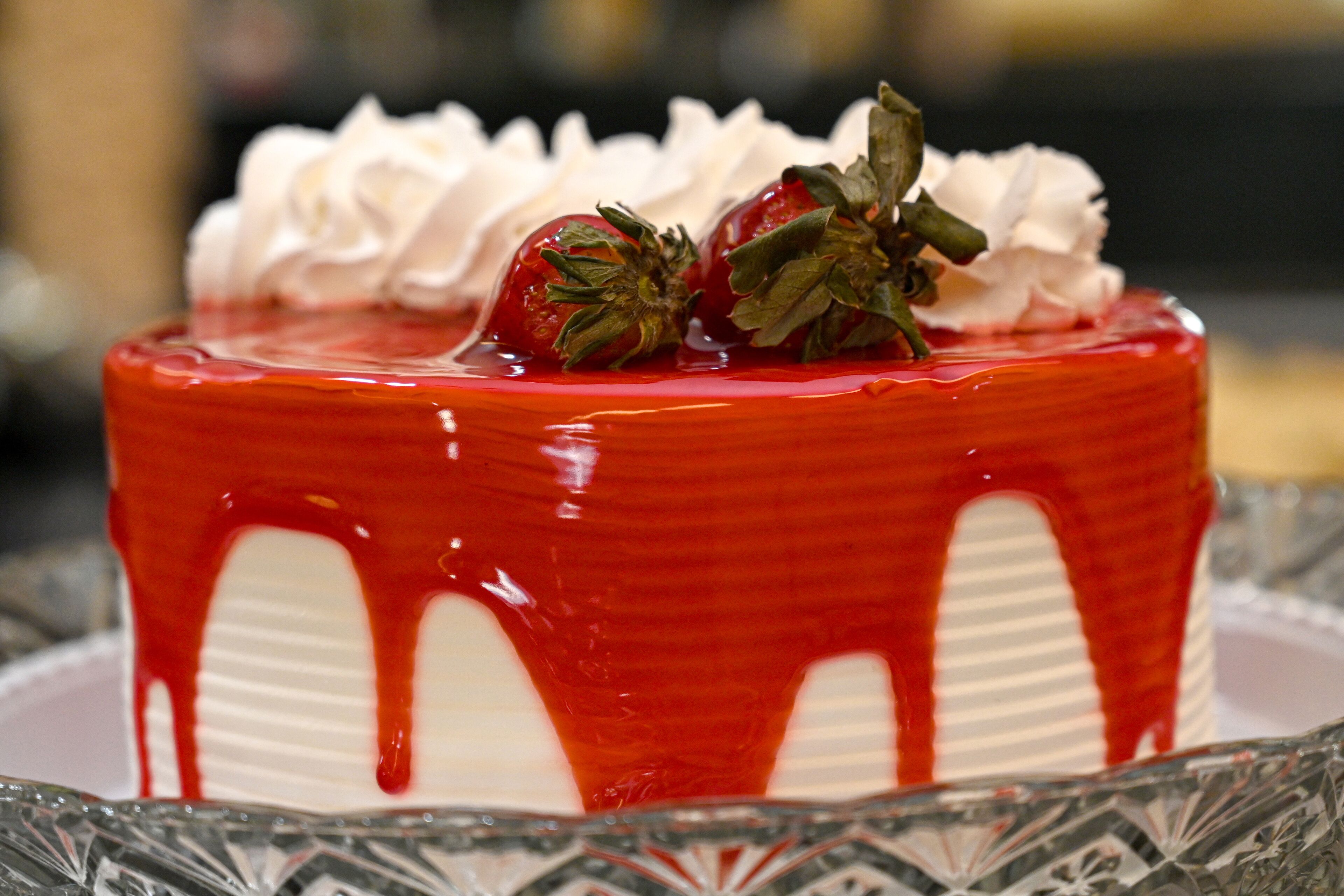 Una torta con fragole e panna montata, irrorata da salsa rossa.