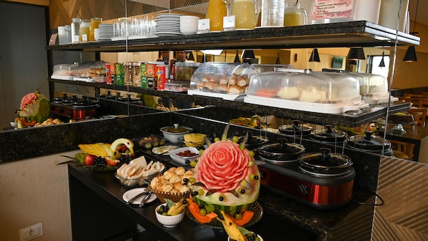 A buffet with various food items, including a watermelon with a rose carved into it, and multiple serving dishes and containers. - Pousada Galemares (Maragogi)