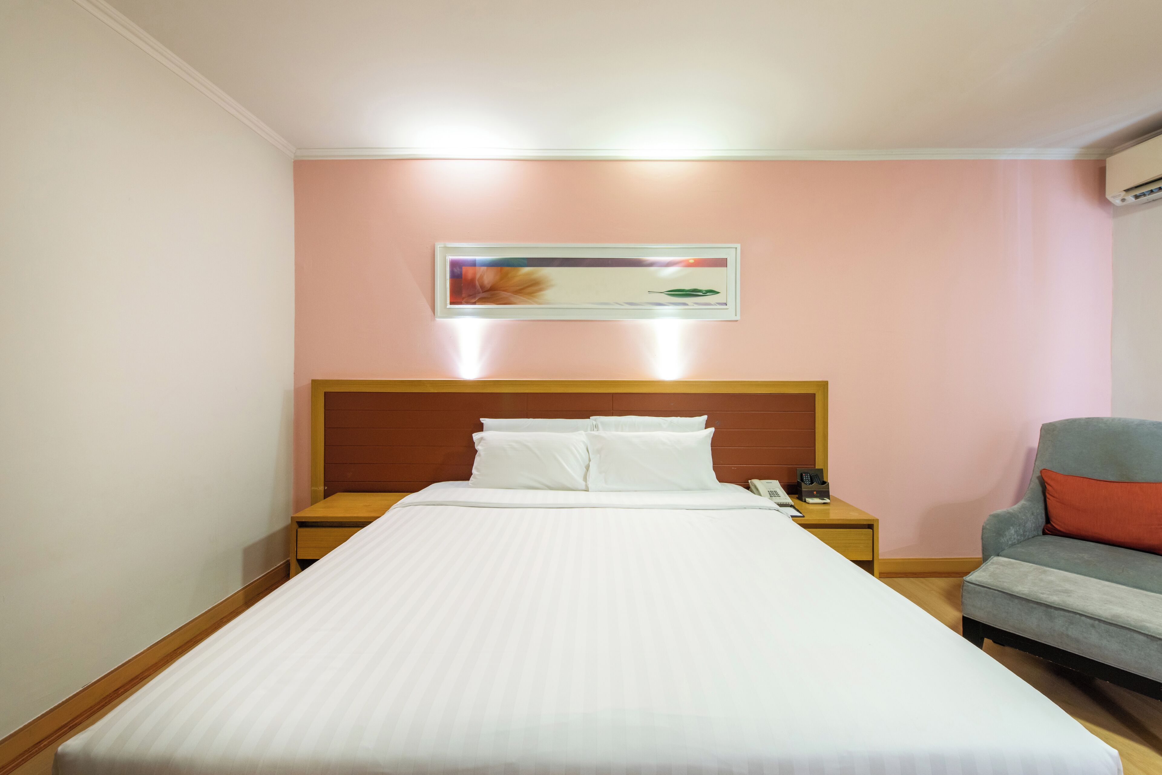 A hotel room with a bed, a nightstand, a chair, and a wall-mounted artwork.