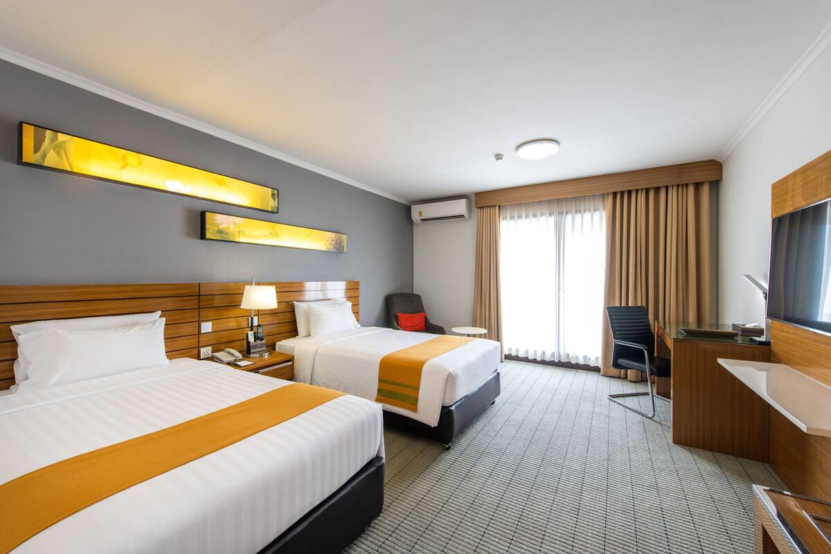 A hotel room with two beds, a desk, a chair, a TV, and a window with curtains.