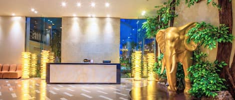 Un área de recepción con mostrador de mármol, una gran escultura de elefante dorado y una pared con plantas.